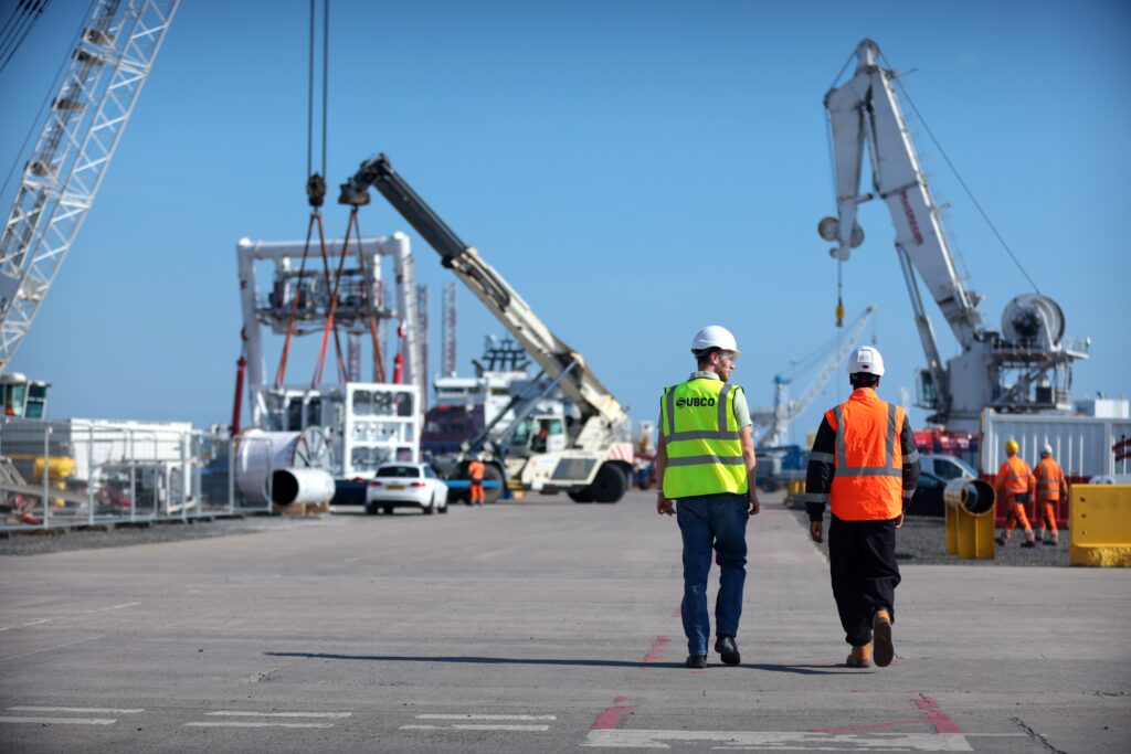 Two workers in high-viz vests walking next to engineering cranes